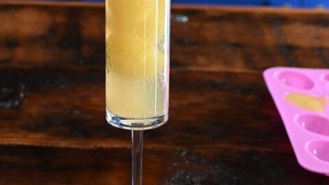 orange juice ice cubes being placed in champagne flute for Easter Mimosas