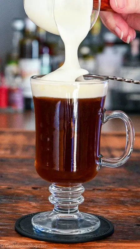 white whipped cream being poured on top of coffee in glass mug