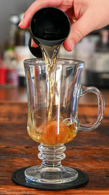 Whiskey being poured in glass mug with a jigger