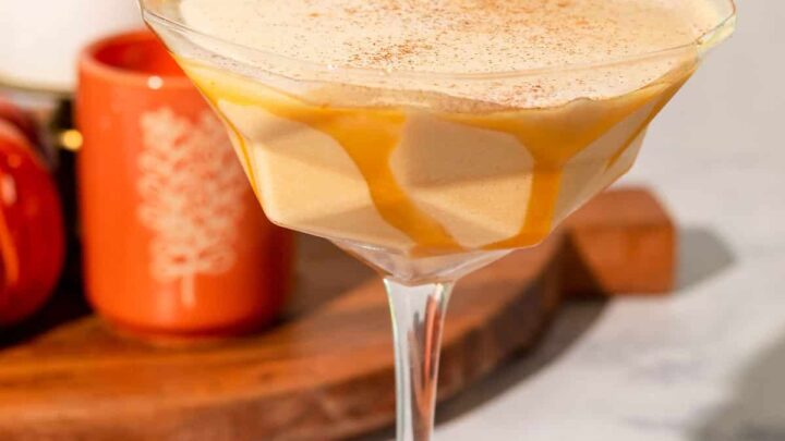 tan cocktail in coupe with caramel sauce garnish and cinnamon stick on rim