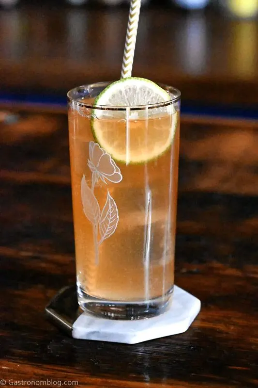 tan Kentucky Horsefeather Cocktail in tall glass with rose etched, lime slice and straw