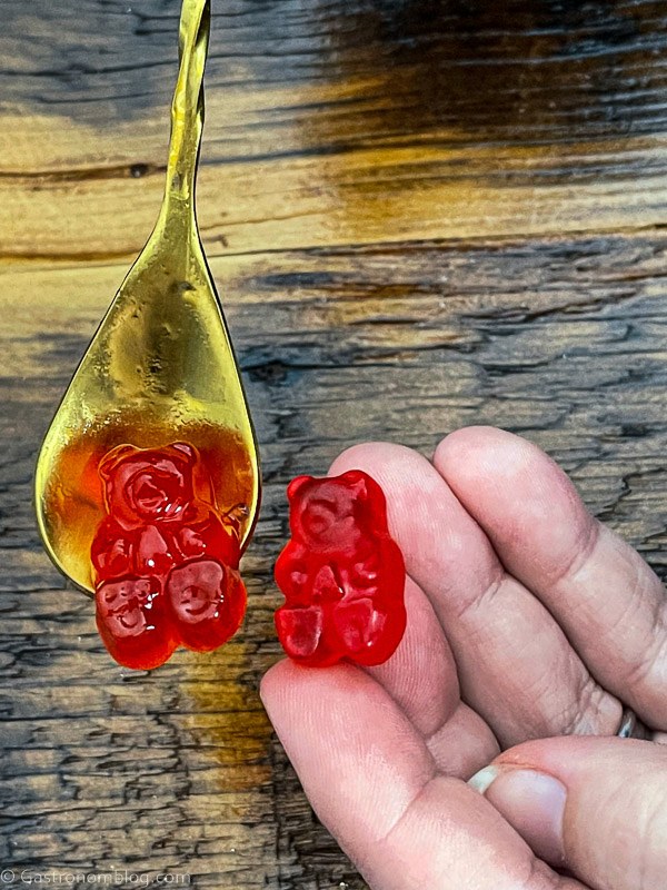 Gold spoon with red gummy bear, hand holding red gummy bear