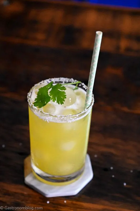 Yellow cocktail with pineapple wedge garnish, straw and cilantro - Pineapple Cilantro Margaritas