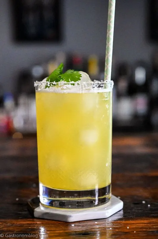 Yellow cocktail with pineapple wedge garnish, straw and cilantro - Pineapple Cilantro Margaritas