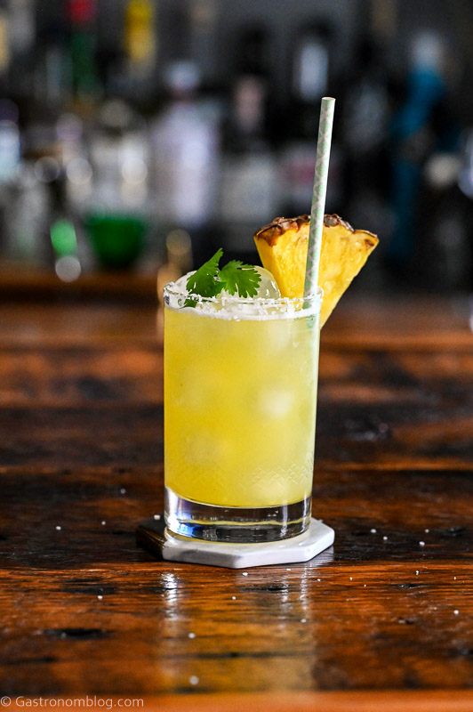 Yellow cocktail with pineapple wedge garnish, straw and cilantro - Pineapple Cilantro Margaritas