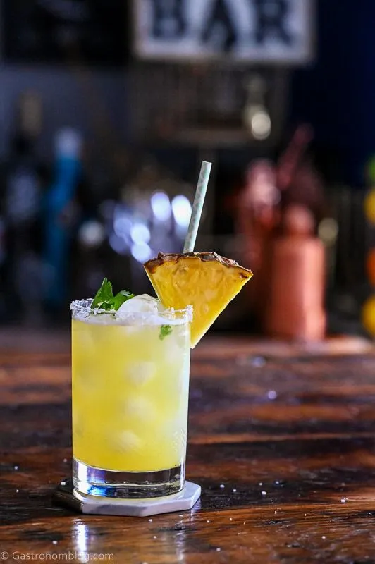 Yellow cocktail with pineapple wedge garnish, straw and cilantro - Pineapple Cilantro Margaritas