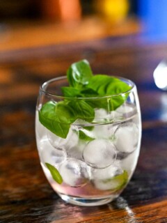 Pink Rhubarb Cocktail in glass with ice balls and basil garnish