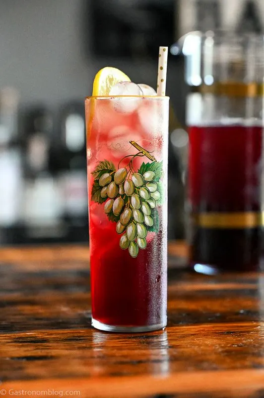 Purple grape lemonade cocktail in tall glass with green grapes print on wooden table