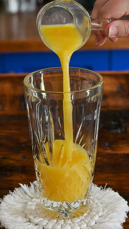 orange juice being poured into a glass shaker.
