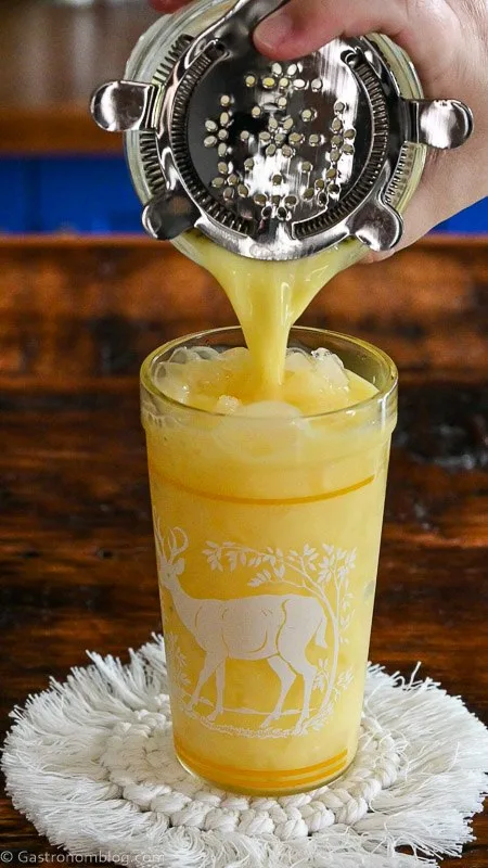 orange citrus fizz being poured from shaker into glass with a deer on a white coaster.