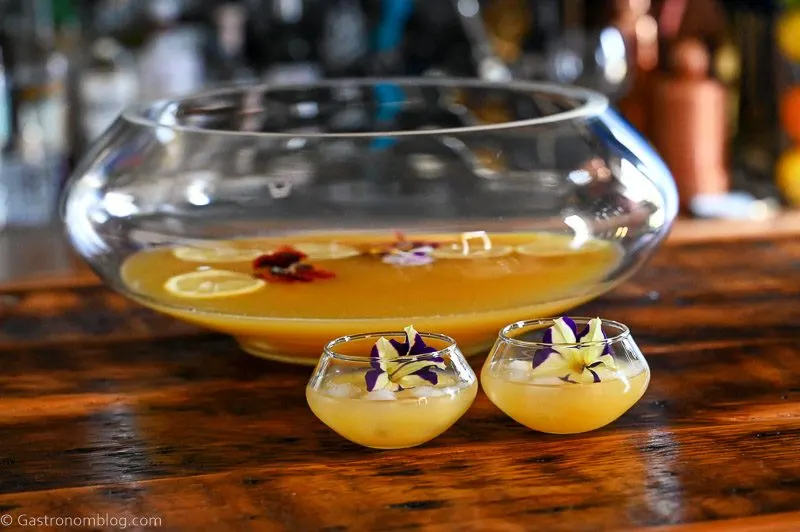 Yellow Pineapple Wine Punch in punch cups with edible flower, punch bowl behind
