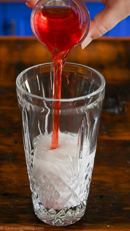 strawberry syrup being poured into glass cocktail shaker