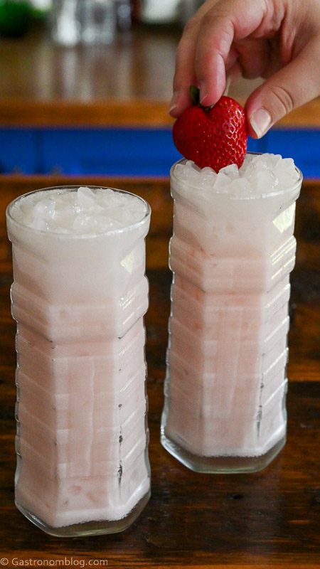 light pink Strawberry Coconut cocktails in highball glasses with a strawberry garnish