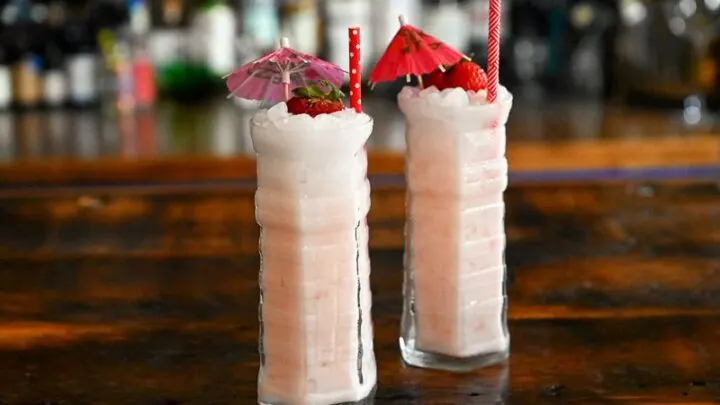 light pink Strawberry Coconut cocktails in highball glasses with a strawberry garnish and umbrellas