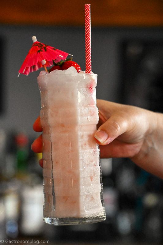 hand holding light pink Strawberry Coconut cocktails in highball glasses with a strawberry garnish and umbrellas