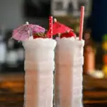 light pink Strawberry Coconut cocktails in highball glasses with a strawberry garnish and umbrellas