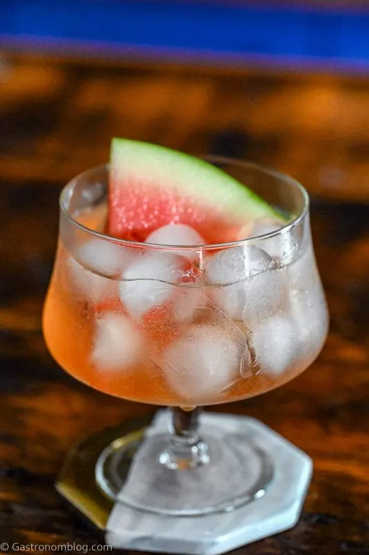 Pink cocktail, Watermelon Aperol Spritz in a low glass with stem on wood table. Ice cubes in glass with watermelon slice