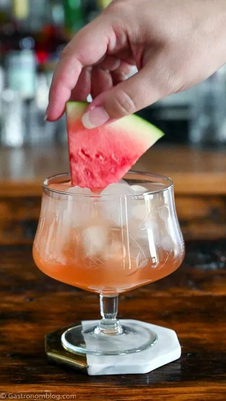watermelon being placed in glass with ice and pink liquid