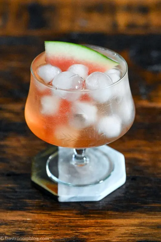 Pink cocktail, Watermelon Aperol Spritz in a low glass with stem on wood table. Ice cubes in glass with watermelon slice