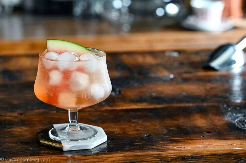 Pink cocktail, Watermelon Aperol Spritz in a low glass with stem on wood table. Ice cubes in glass with watermelon slice