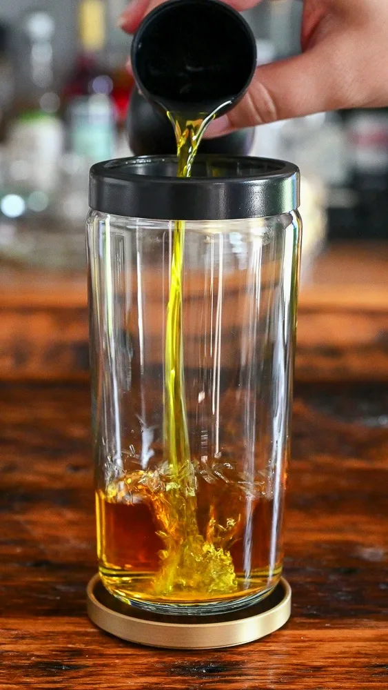 yellow Strega being poured into a glass cocktail shaker