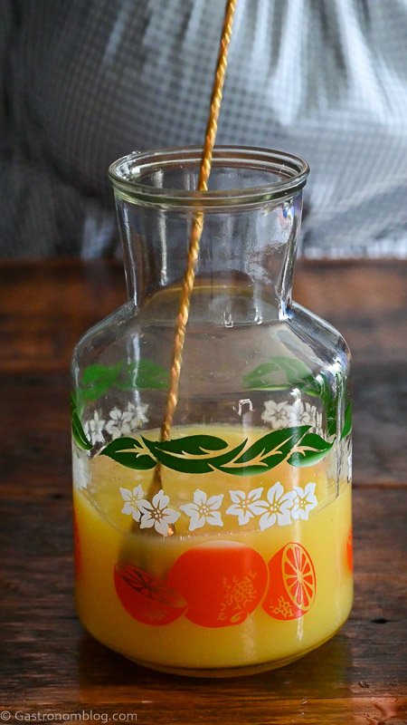 long gold bar spoon stirring juice in orange printed pitcher
