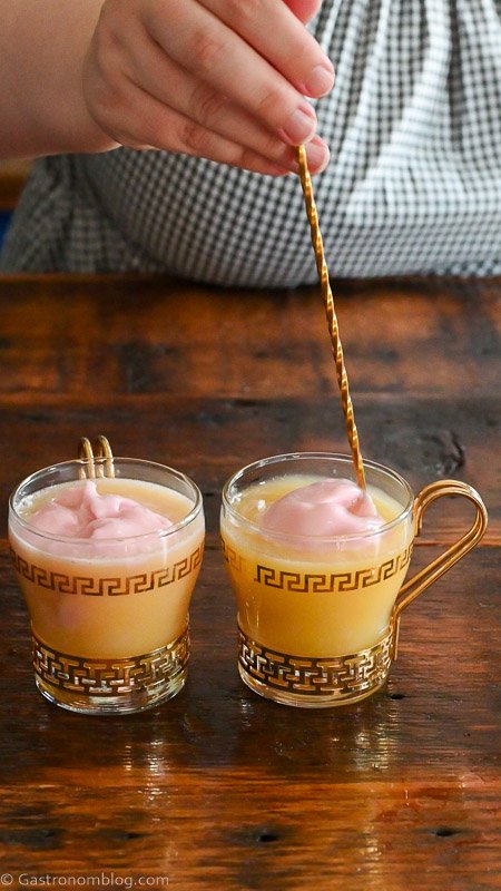 long gold bar spoon stirring orange juice in gold trimmed punch cup with raspberry sherbet on top