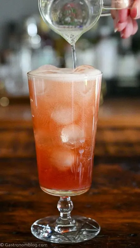 prosecco being poured into tall glass filled with ice and pink cocktail