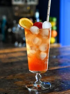 pink Strawberry Aperol Spritz cocktail with ice balls, orange slice and strawberry in tall glass on wood table