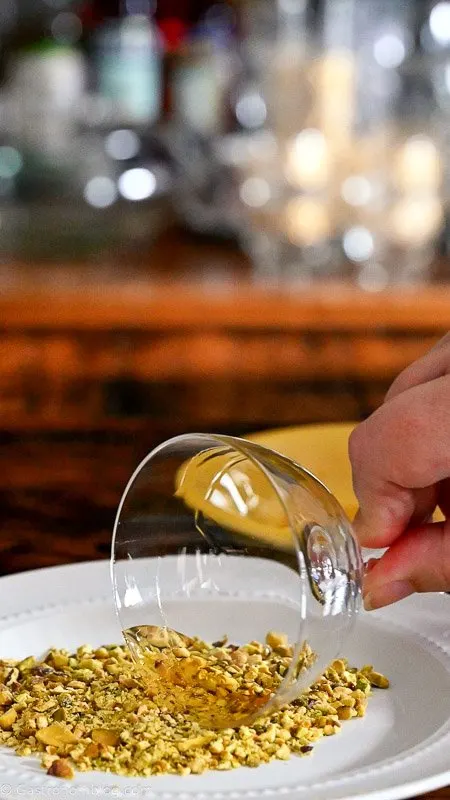 Cocktail coupe being dipped in pistachios on a white plate