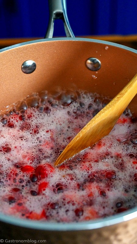 stirring cranberries floating in syrup in copper saucepan