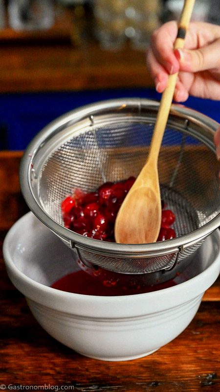 pressing down on cranberries in sieve with wooden spoon