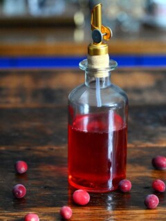 Red cranberry simple syrup in bottle, cranberries around bottle