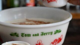 Tom and Jerry Drink in a large ceramic punch bowl, hand pouring batter from punch bowl into a mug