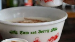 Tom and Jerry Drink in a large ceramic punch bowl, hand pouring batter from punch bowl into a mug