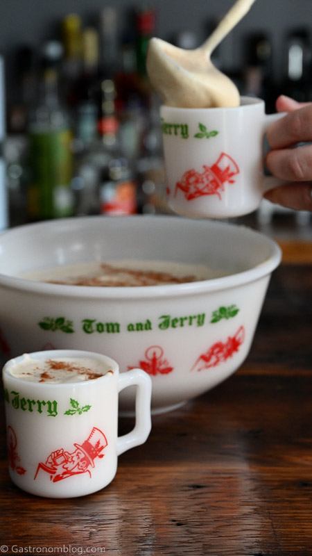 Tom and Jerry Drink in a large ceramic punch bowl, hand pouring batter from punch bowl into a mug