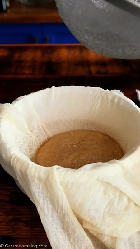 straining tan hazelnut orgeat through cheesecloth