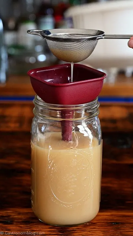 pouring tan hazelnut orgeat into a jar using a purple funnel