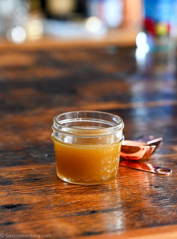 tan pistachio orgeat syrup in jar, copper measuring spoon on wood table