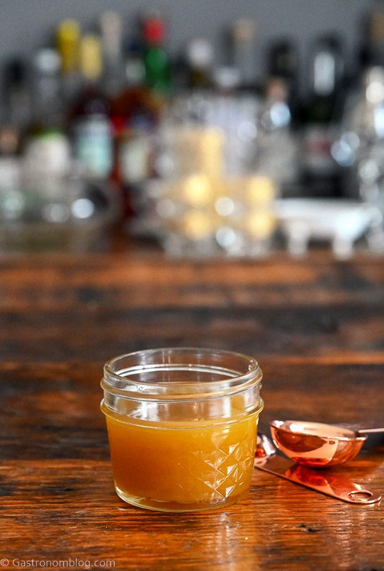 tan pistachio orgeat syrup in jar, copper measuring spoon on wood table