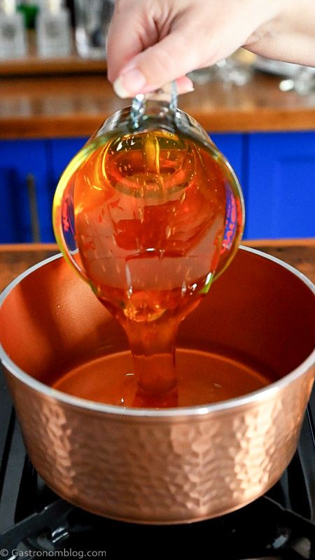 pouring honey from glass measuring cup into a copper saucepan