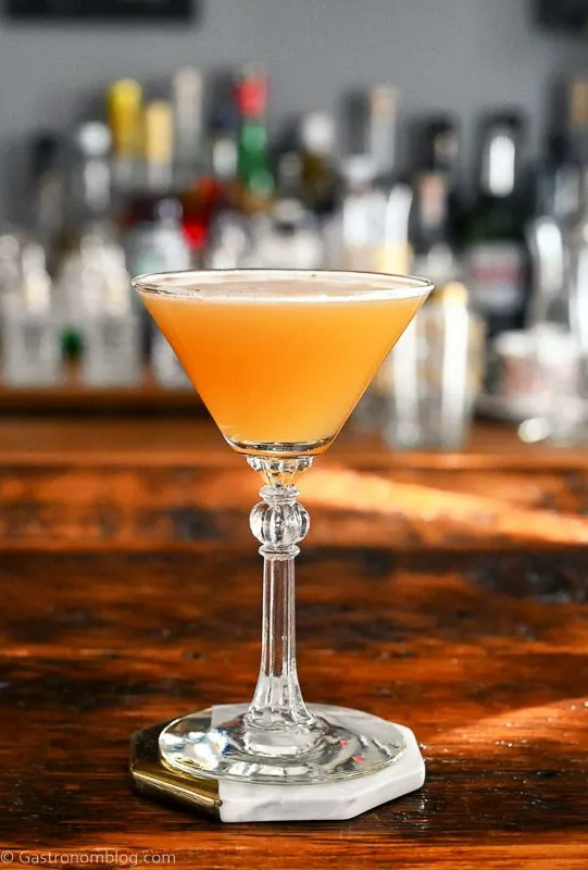 pineapple whiskey cocktail in cocktail coupe. Gold colored cocktail on wood table.