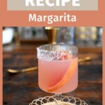 pink grapefruit margarita cocktail in stemmed glass on wicker coaster on wood table