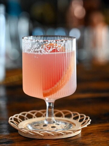 pink grapefruit margarita cocktail in stemmed glass on wicker coaster on wood table