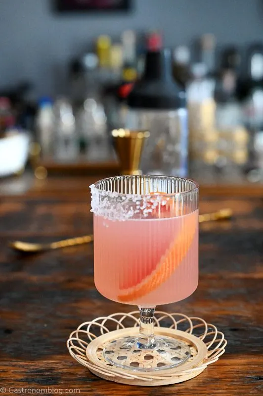 pink grapefruit margarita cocktail in stemmed glass on wicker coaster on wood table