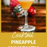 pineapple whiskey cocktail in cocktail coupe. Gold colored cocktail on wood table.