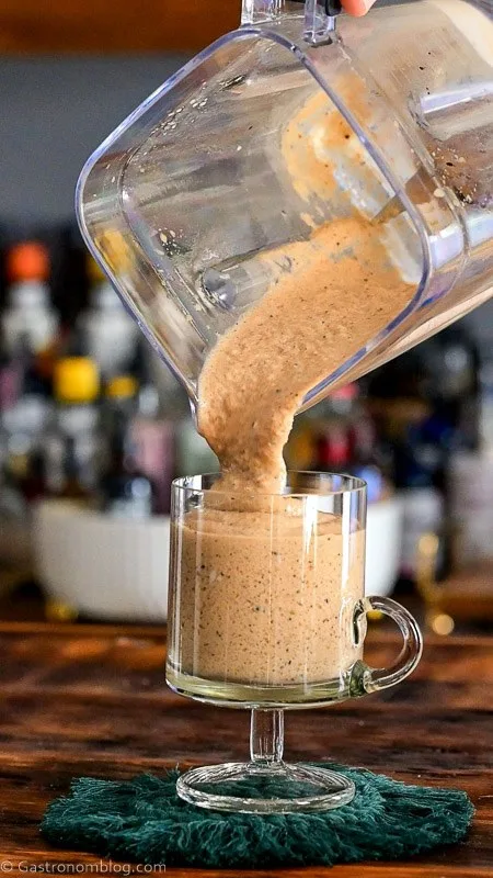 pouring tan milkshake into footed glass mug