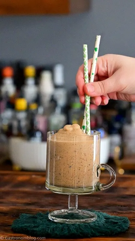 putting St. Patrick's Day straws into tan cocktail in glass footed mug