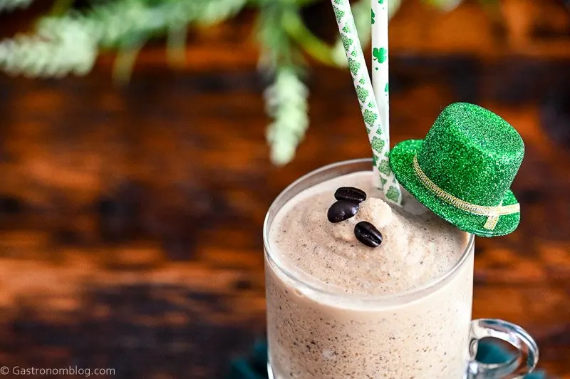 tan cocktail in footed glass mug, this Frozen Irish Coffee has St Patrick's Day straws, hat and greenery behind