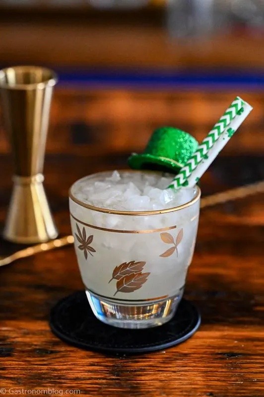 Irish Mule cocktail in gold leaf rocks glass with St Patricks Day clover straws and hat garnish, gold barware behind